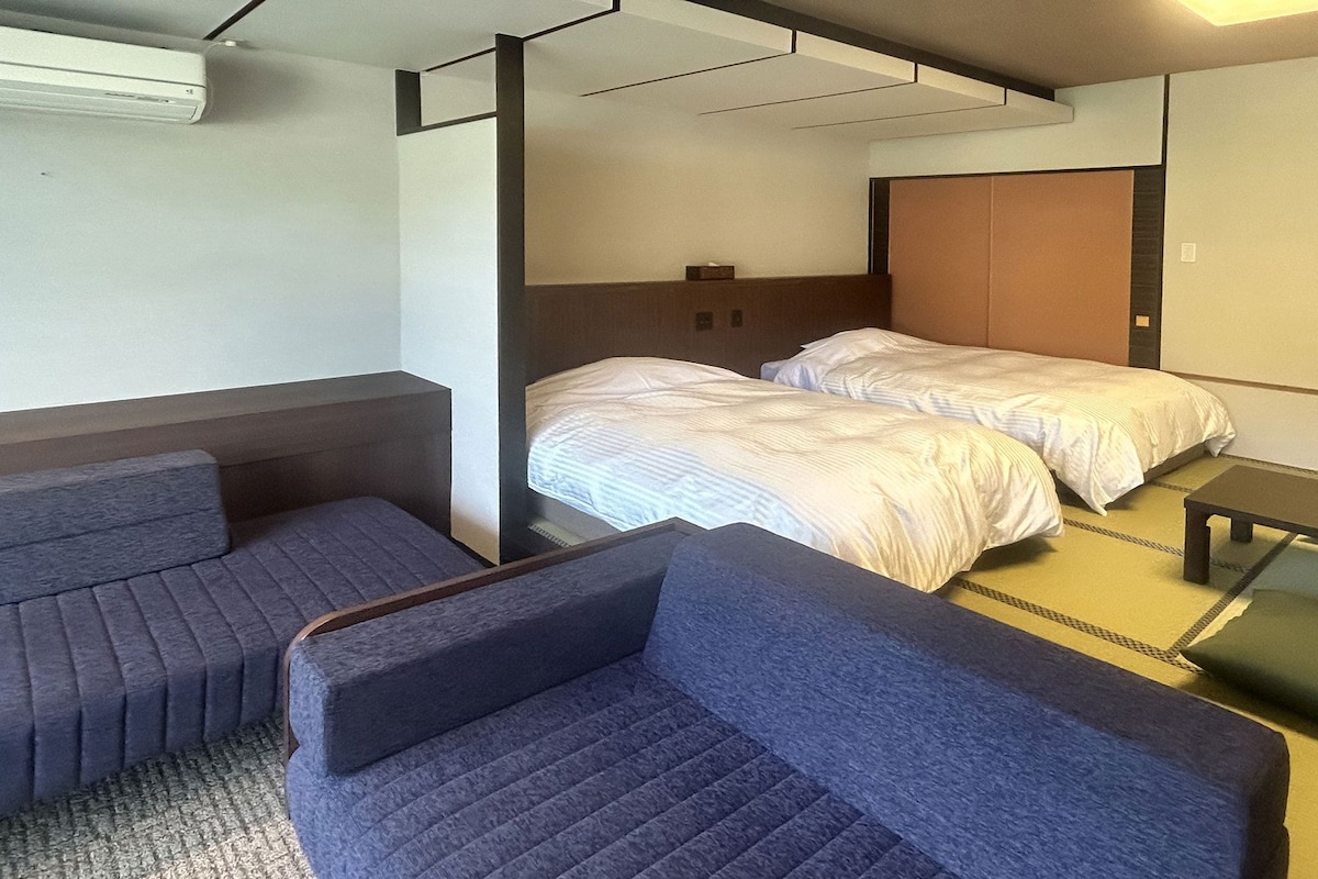 A hotel room with two beds, a sofa, a desk, and a partition wall.