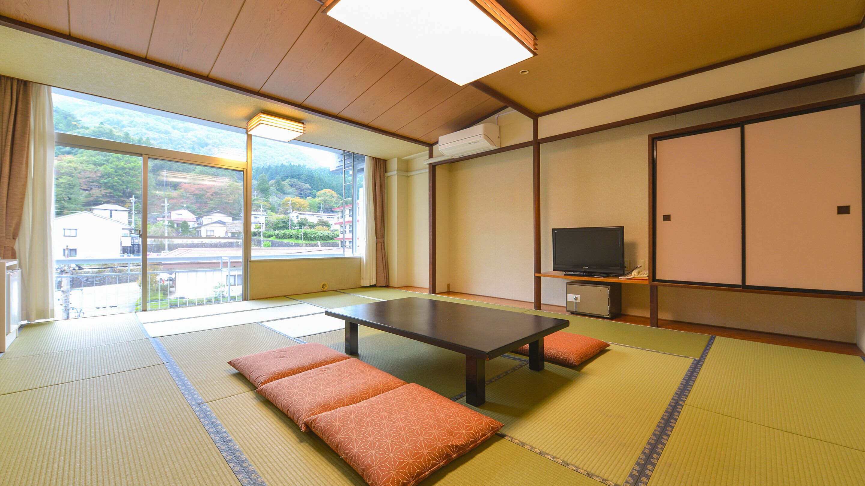 Una habitación japonesa tradicional con suelo de tatami, una mesa baja, cojines, un televisor y una puerta corredera.