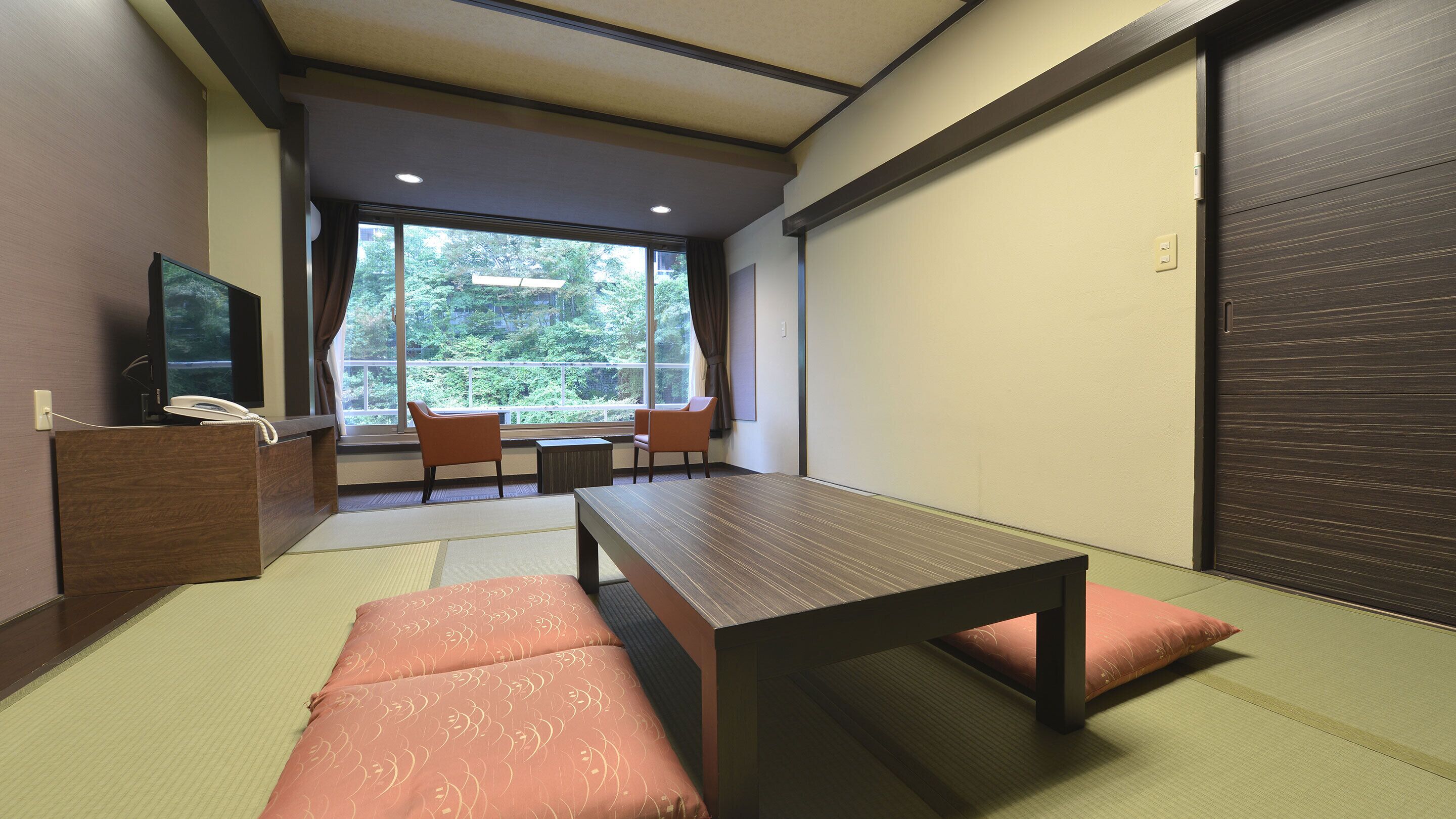 Habitación con esteras de tatami, una mesa baja, dos sillas, una mesita con un teléfono y una puerta corrediza.