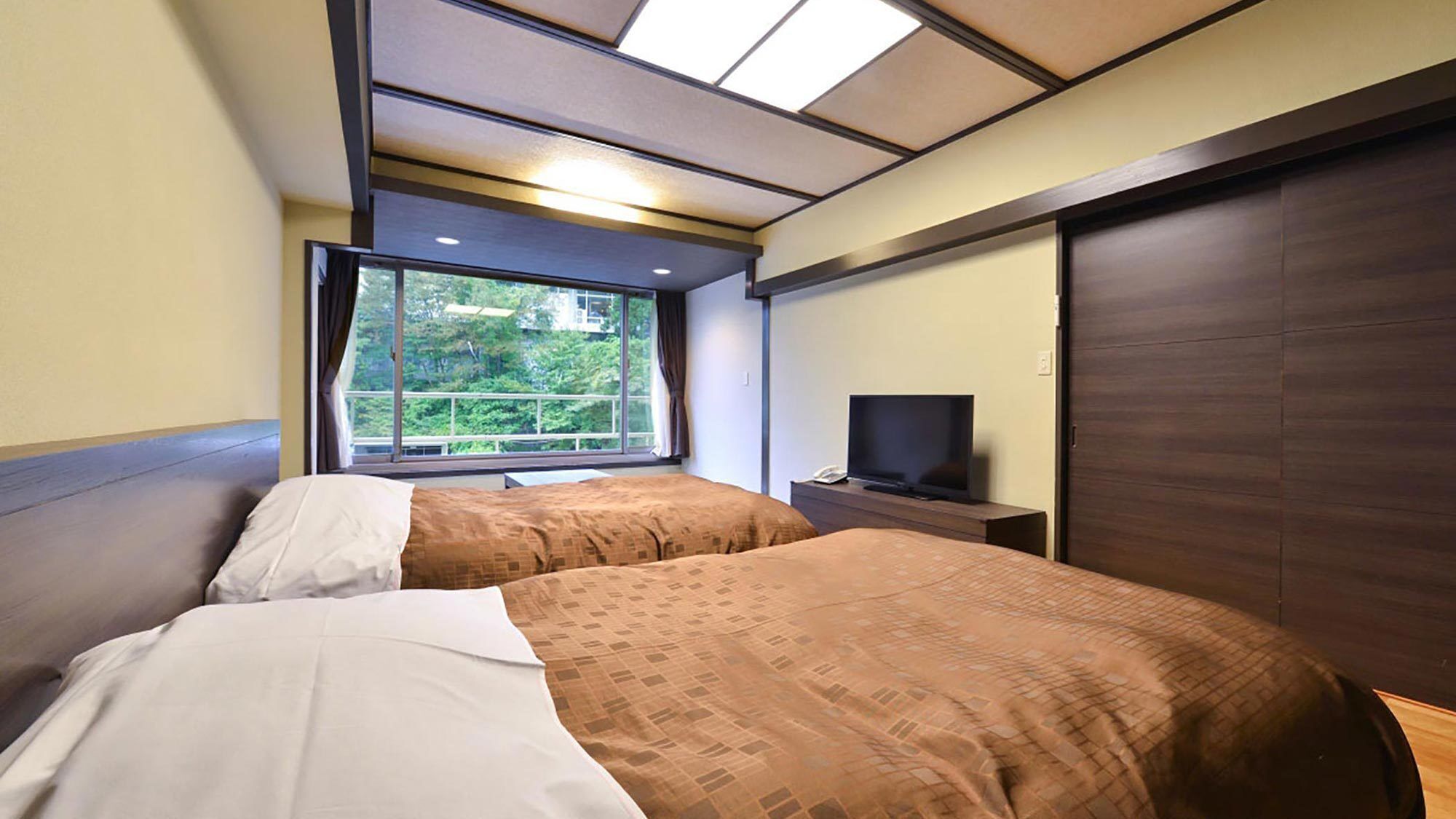 Habitación de hotel con dos camas, televisión, ventana con vista a zonas verdes y puerta corredera.
