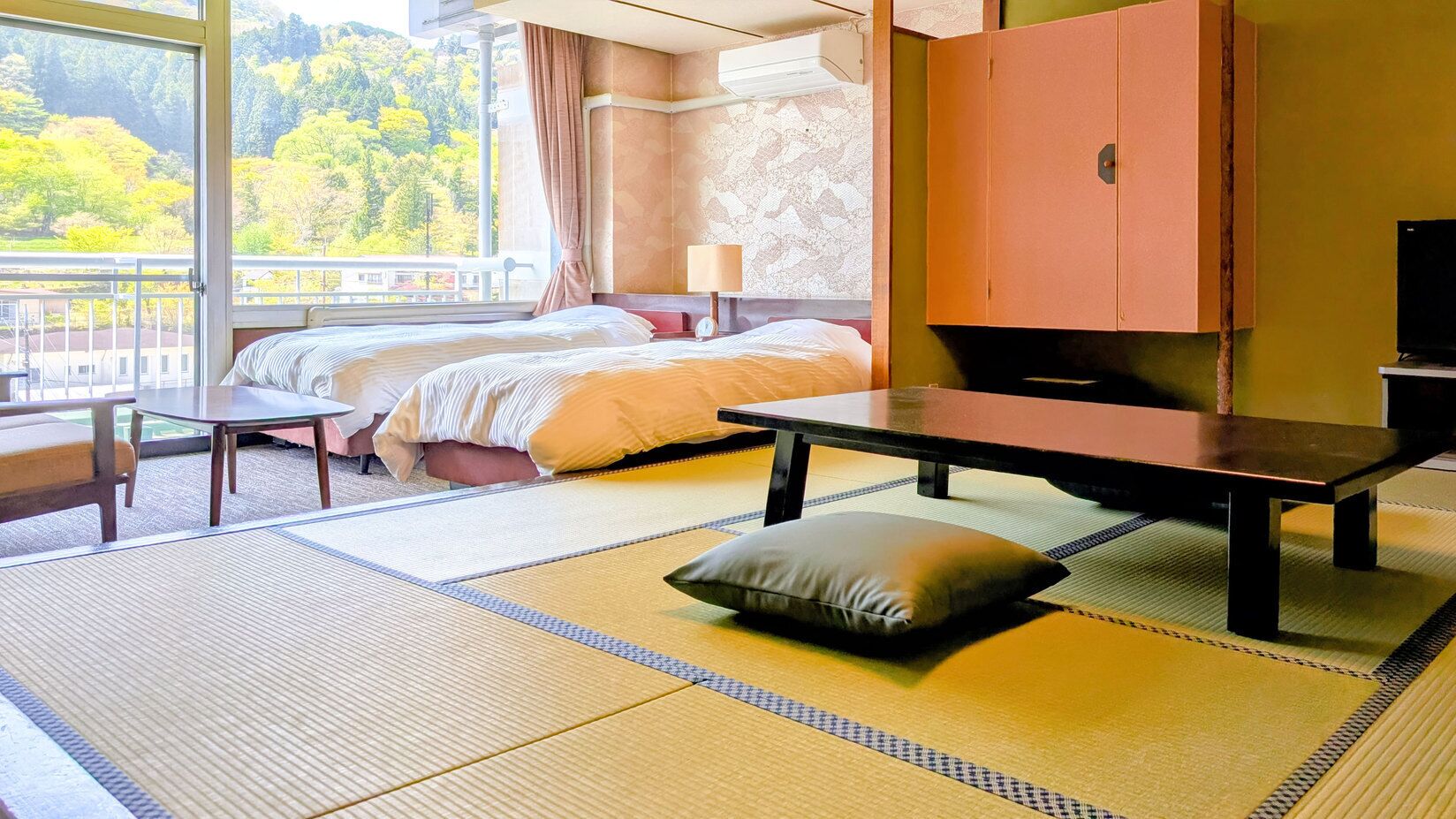 Una habitación japonesa tradicional con suelo de tatami, una cama, una mesa y vistas a un bosque.