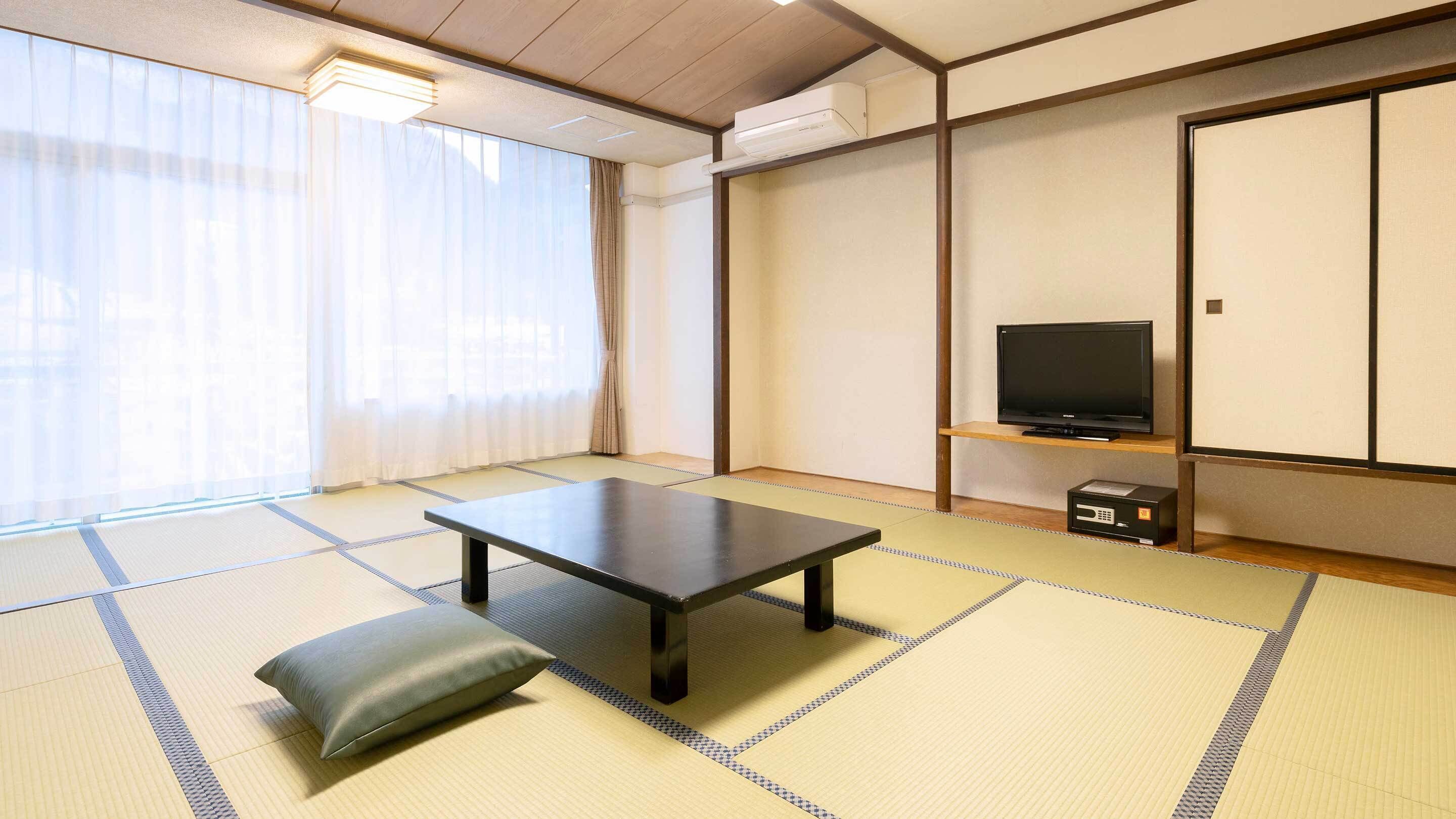 Une pièce avec un sol recouvert de tatamis, une petite table basse, un coussin, un téléviseur posé sur une étagère et une porte coulissante.
