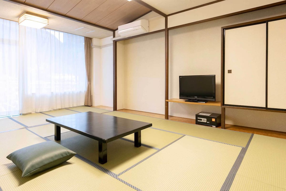A room with tatami flooring, a low table, a cushion, a television on a shelf, and a sliding door.