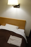 Una cama bien hecha con cabecera de madera, almohada blanca y manta a rayas doblada.