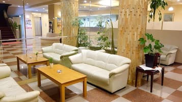 A lobby with a checkered floor, a white sofa, a wooden coffee table, and a potted plant.