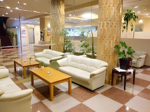 A lobby with a checkered floor, a white sofa, a wooden coffee table, and a potted plant. - Nakamura Prince Hotel (Shimanto)