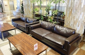 A lobby area with a brown leather sofa, a wooden table, and a no-smoking sign. - Nakamura Prince Hotel (Shimanto)