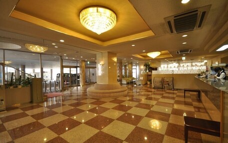 A spacious lobby with a checkered floor, a central column, and a chandelier.