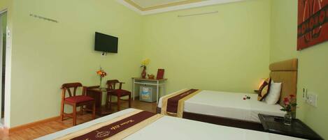 A hotel room with two beds, a desk, a chair, a television, and a ceiling fan.