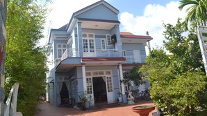 A two-story building with a red-tiled roof, white-framed windows, and a balcony. - Hoi An Life Homestay (Da Nang)