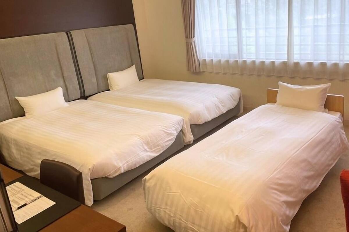 A hotel room with two single beds, a desk with a chair, and a red armchair.