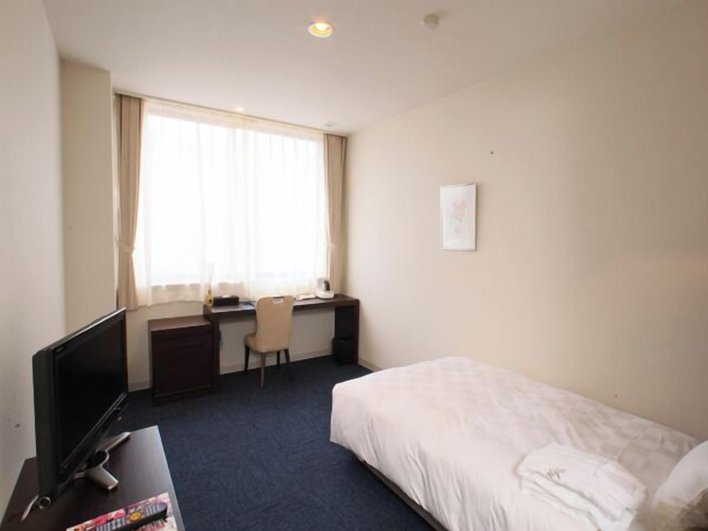 Ein Hotelzimmer mit einem Bett, einem Schreibtisch, einem Stuhl, einem Fernseher und einem Fenster mit Vorhängen.