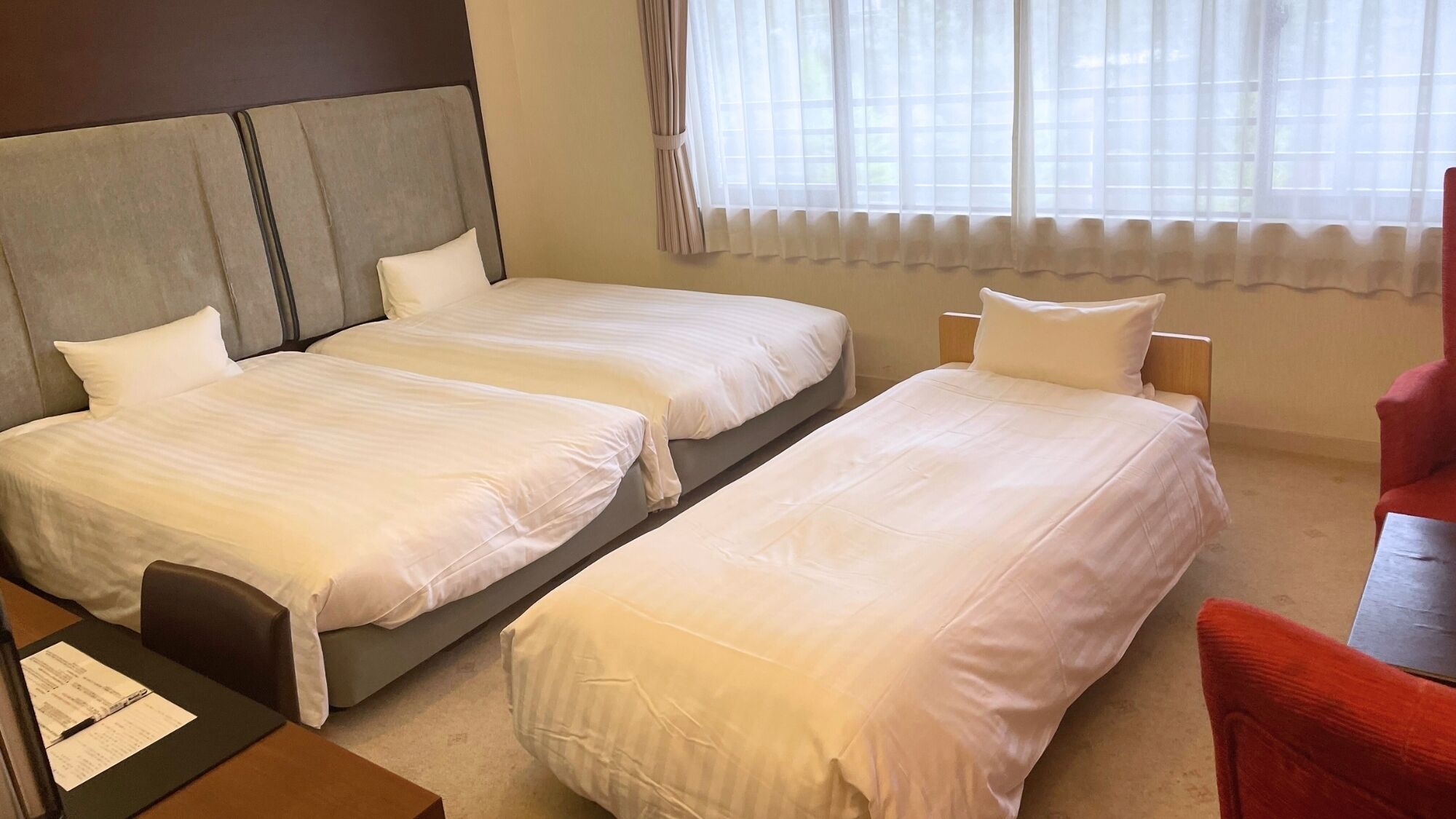 A hotel room with two single beds, a desk with a chair, and a red armchair.