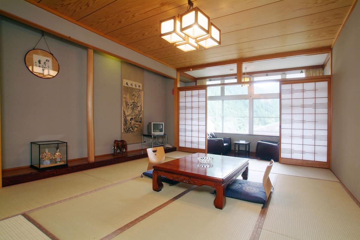 A traditional Japanese room with tatami flooring, a wooden table, a television, and sliding doors.