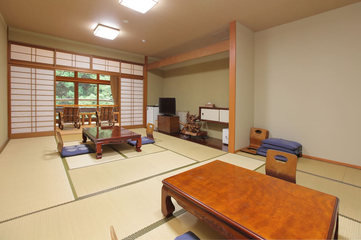 A traditional Japanese room with tatami flooring, a low wooden table, and a television on a cabinet.