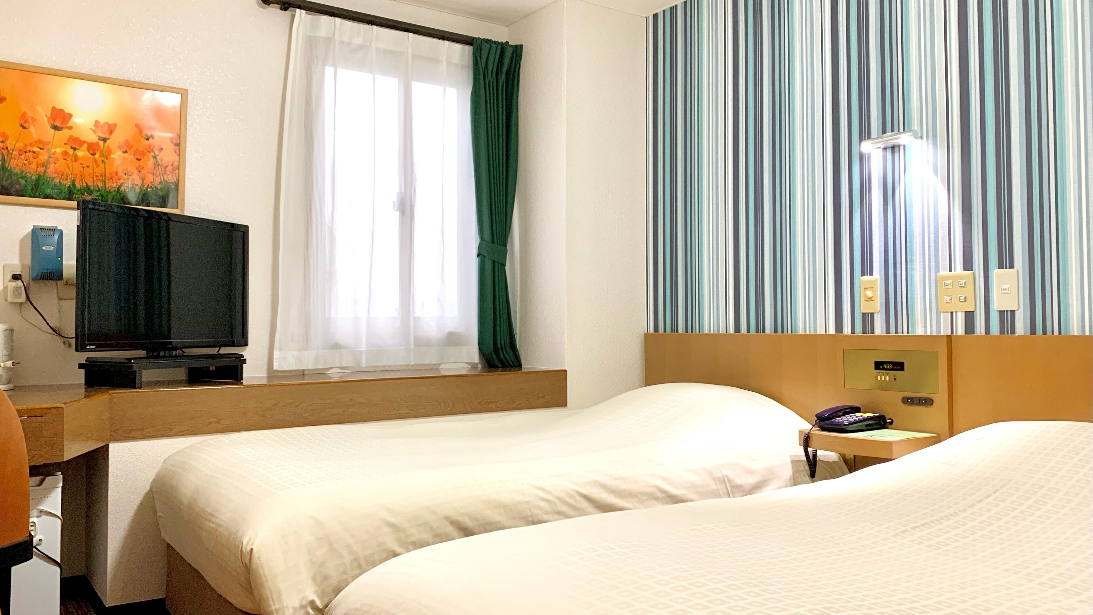 A hotel room with two beds, a television, a window with curtains, a striped wall, and a bedside table with a phone and a lamp.