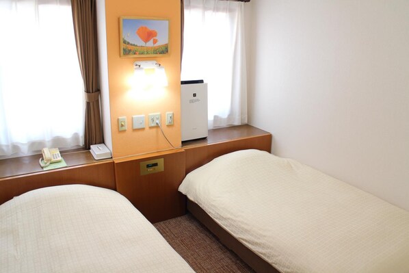 A hotel room with two single beds, a bedside table with a telephone and a power outlet, a wall-mounted heater, and a painting above the heater. - Business Hotel Raicho (Koshigaya)