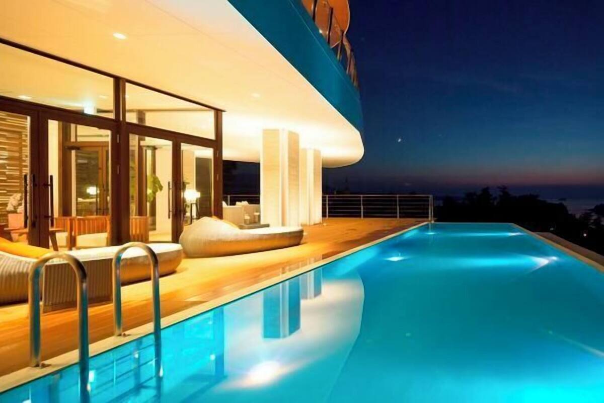 A modern hotel with a swimming pool, large windows, and a view of the ocean at night.