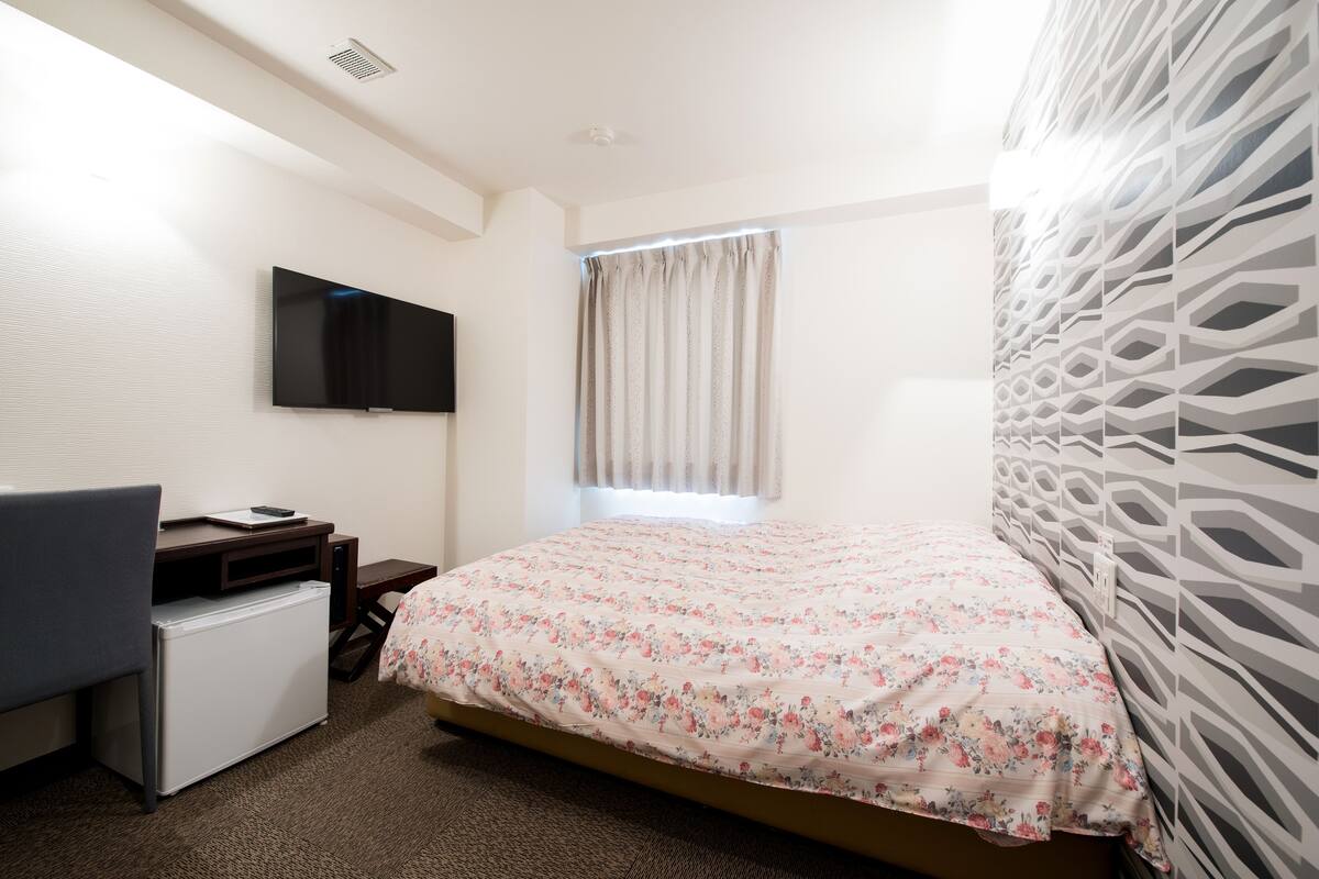 Una habitación de hotel con cama, escritorio con computadora, televisor y ventana con cortinas.