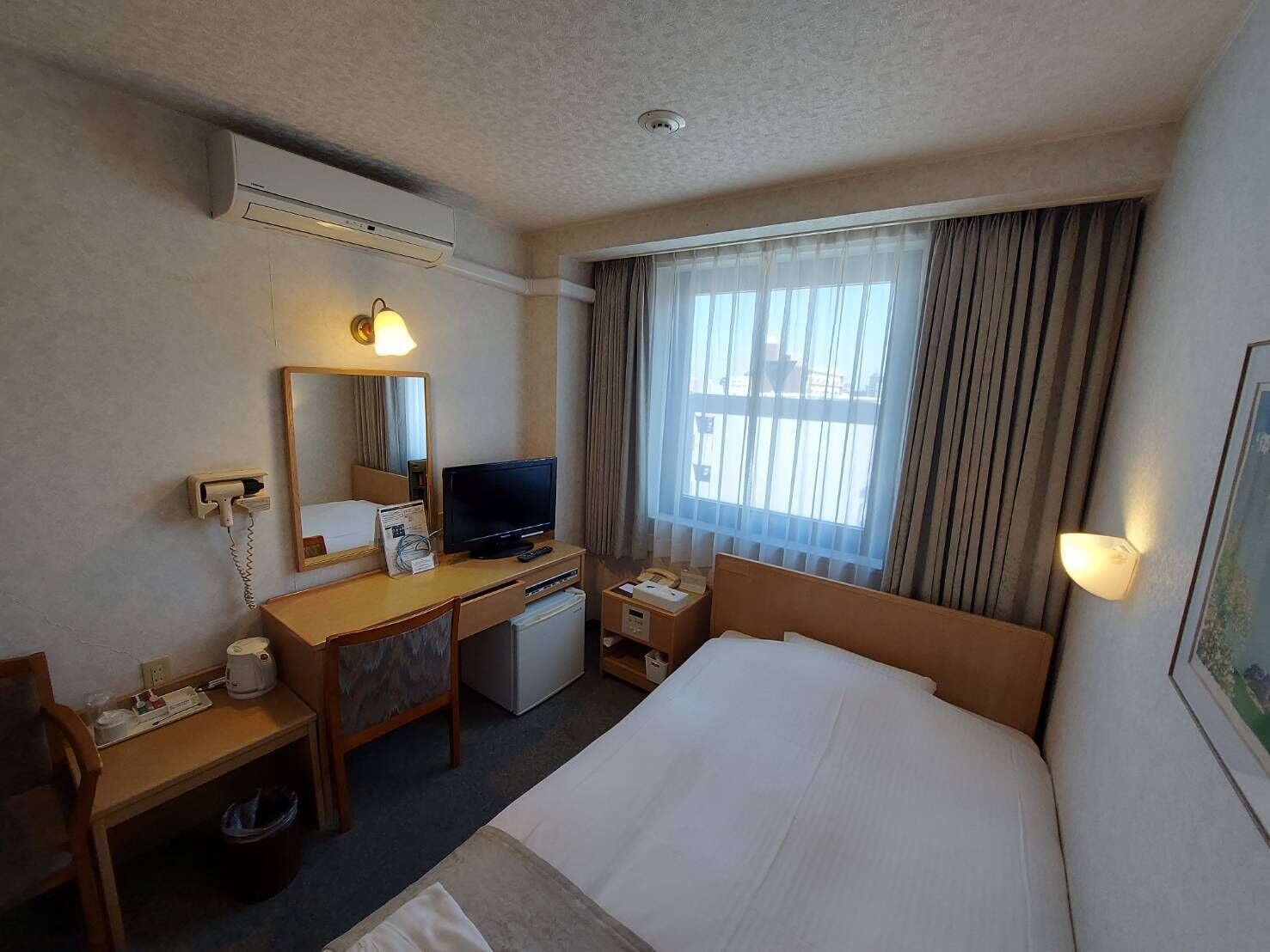 A hotel room with a bed, desk, television, and a window with curtains.
