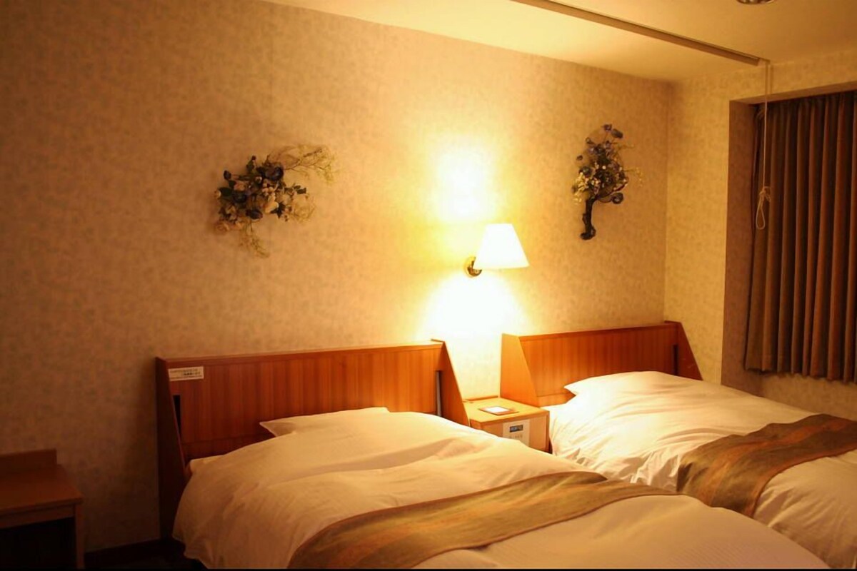 A hotel room with two beds, a nightstand, a lamp, and wall-mounted decor.