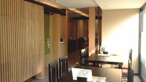 A dining area with a long table and chairs, a wooden partition, and a view of a hallway. - Ibaraki Central Hotel (Ibaraki)