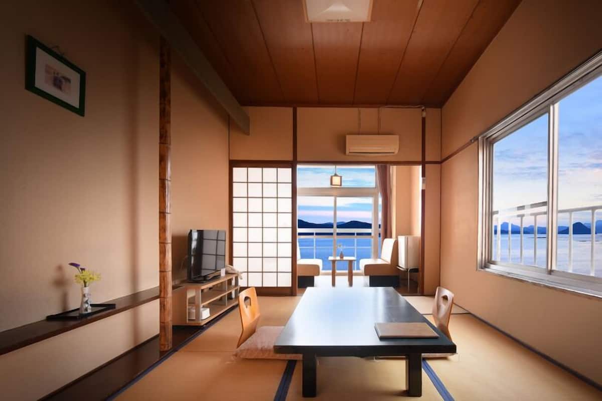 A traditional Japanese room with tatami flooring, a low table, a television, and a view of the sea.