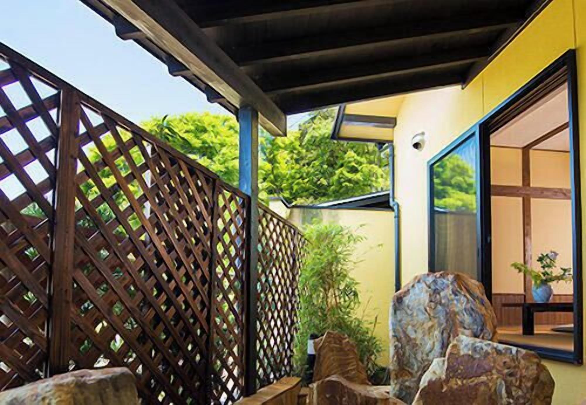 A covered outdoor area with a wooden lattice fence, large rocks, and a view of greenery.