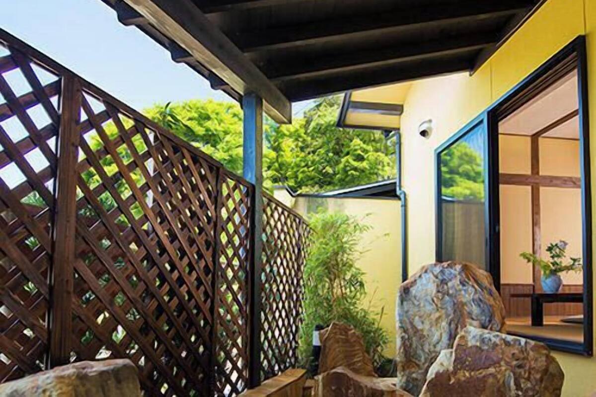 A covered outdoor area with a wooden lattice fence, large rocks, and a view of greenery.