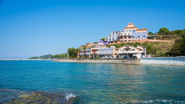 A coastal hotel with multiple buildings, clear blue water, and a rocky shoreline. - Hotel Shoryuen Kaisei (Kamiamakusa)