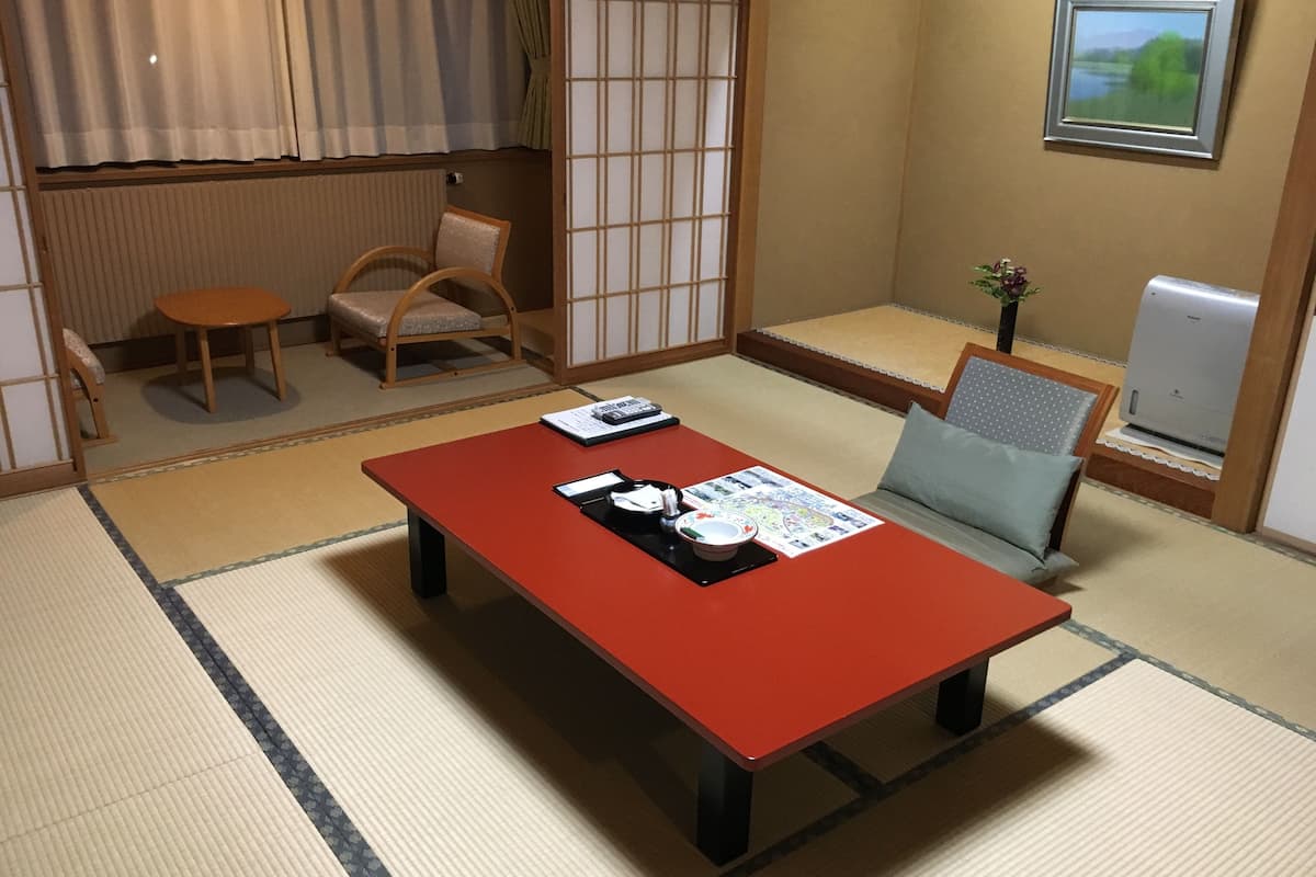 A traditional Japanese room with tatami flooring, a low table with a red top, a chair, and a sofa.