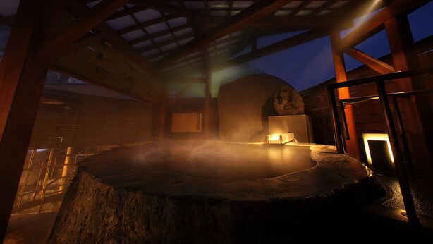 Ein Thermalbad mit einem Steingrundschale, Holzbalken und Blick ins Freie im Dämmerlicht.