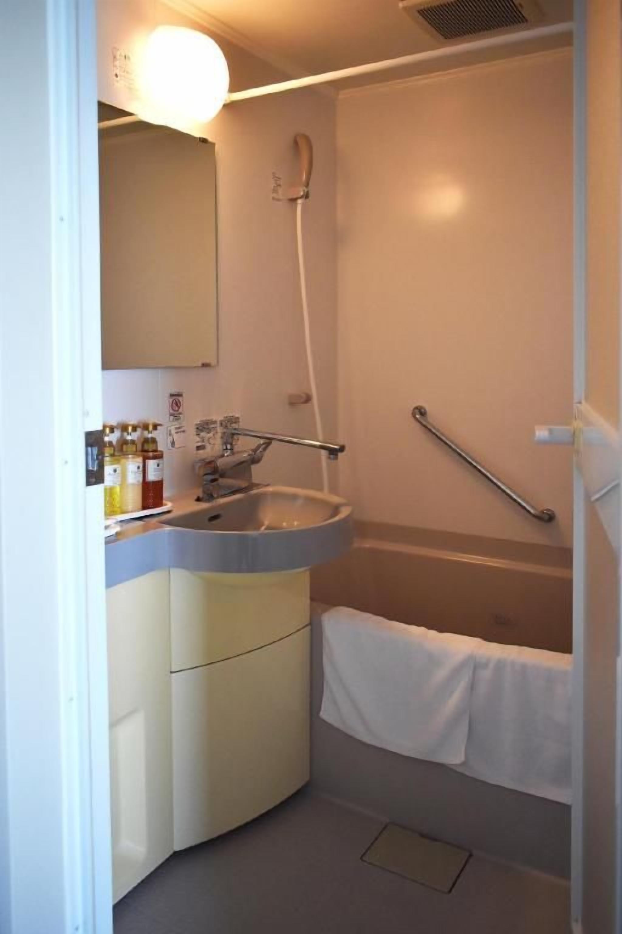 A small bathroom with a sink, mirror, shower, and a towel rack.