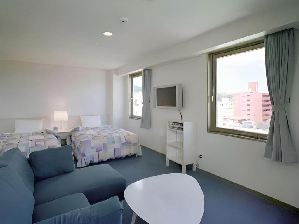 A hotel room with a bed, a sofa, a small table, a TV, and a window with curtains.