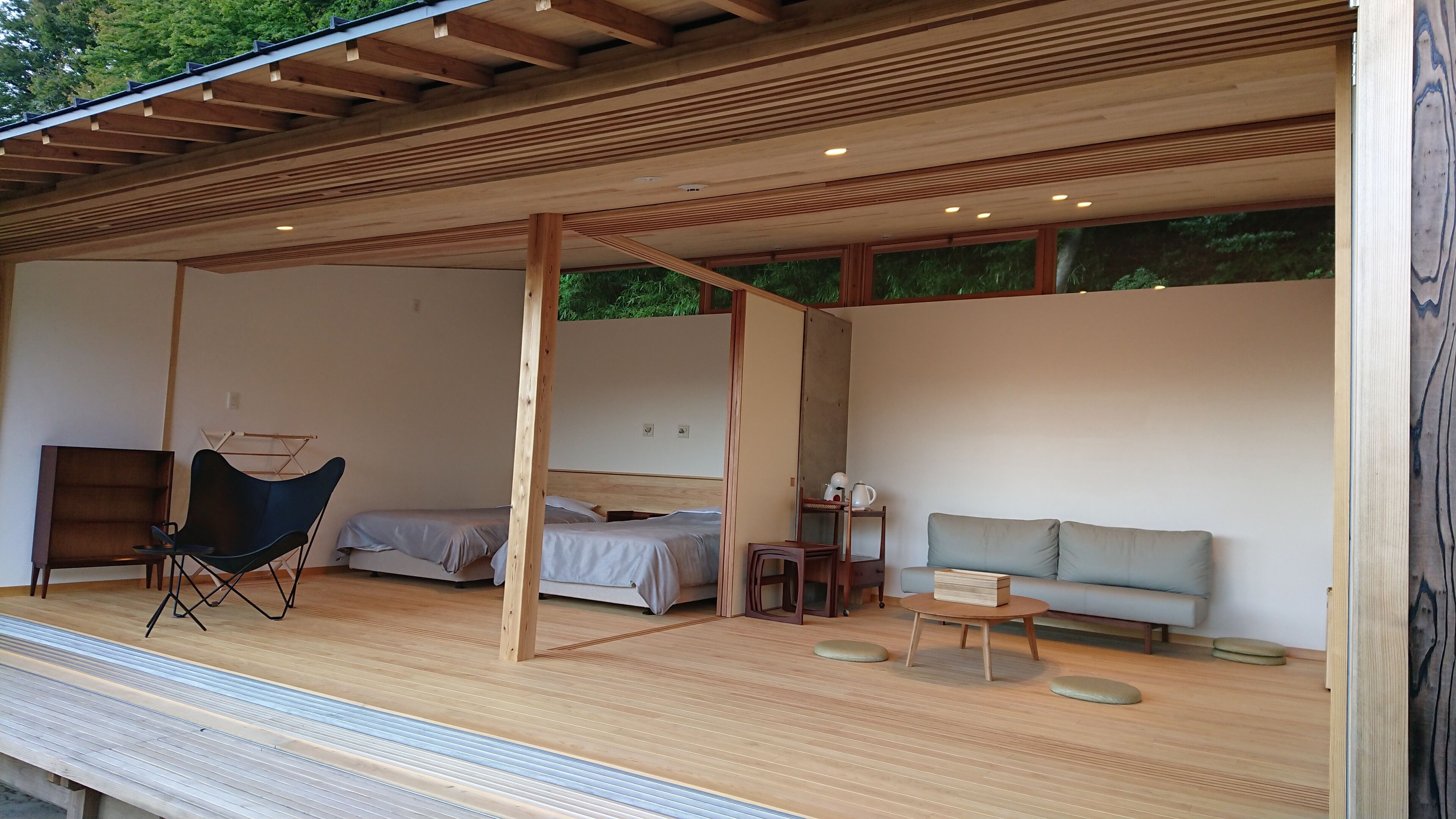 A modern, open-plan room with a bed, a sofa, a chair, and a small table.