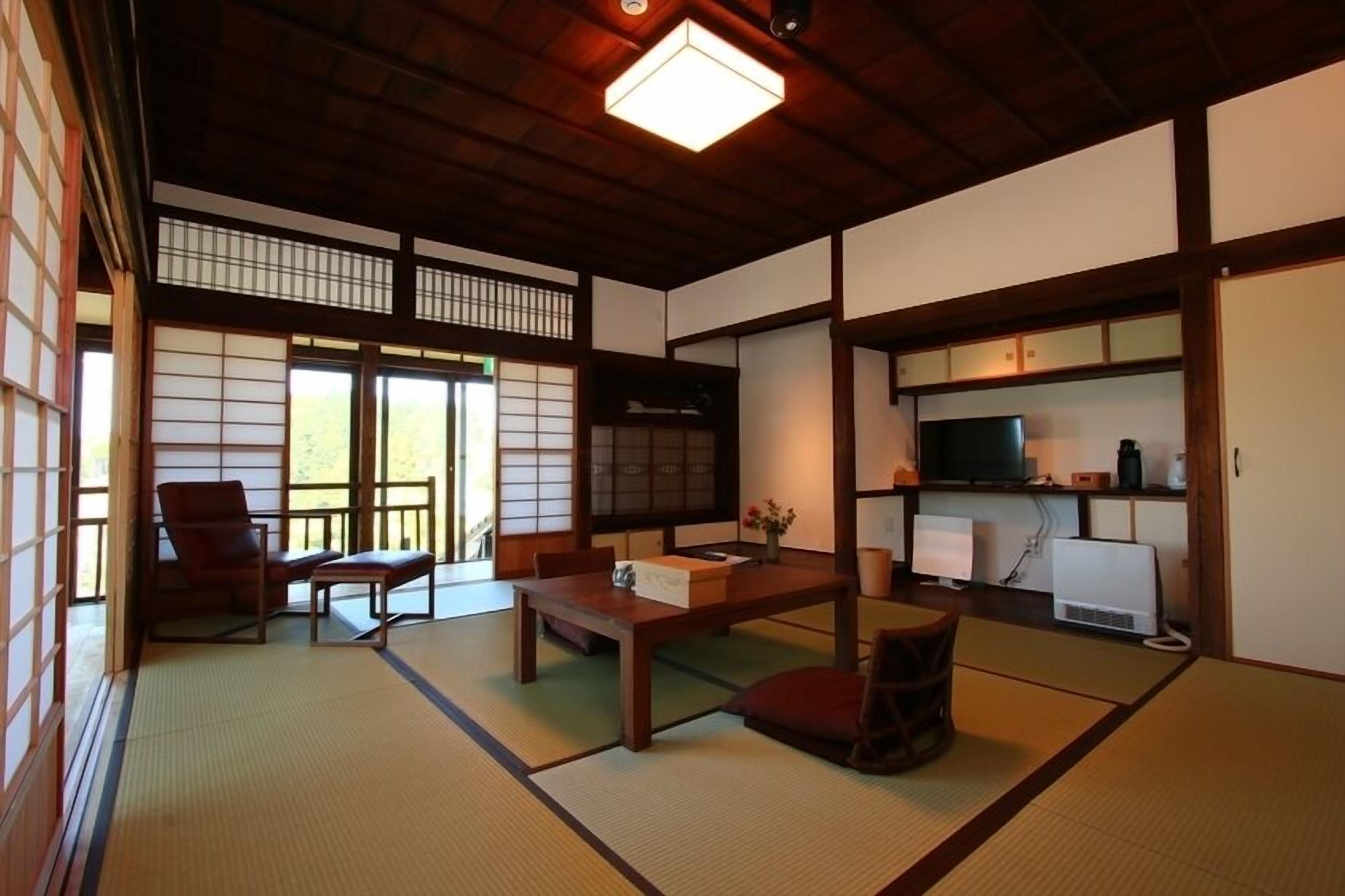 A traditional Japanese room with tatami flooring, a low table, a sofa, a television, and a cabinet with electronic devices.