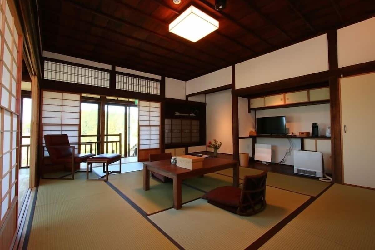 Una habitación japonesa tradicional con suelo de tatami, una mesa baja, un sofá, un televisor y un mueble con dispositivos electrónicos.