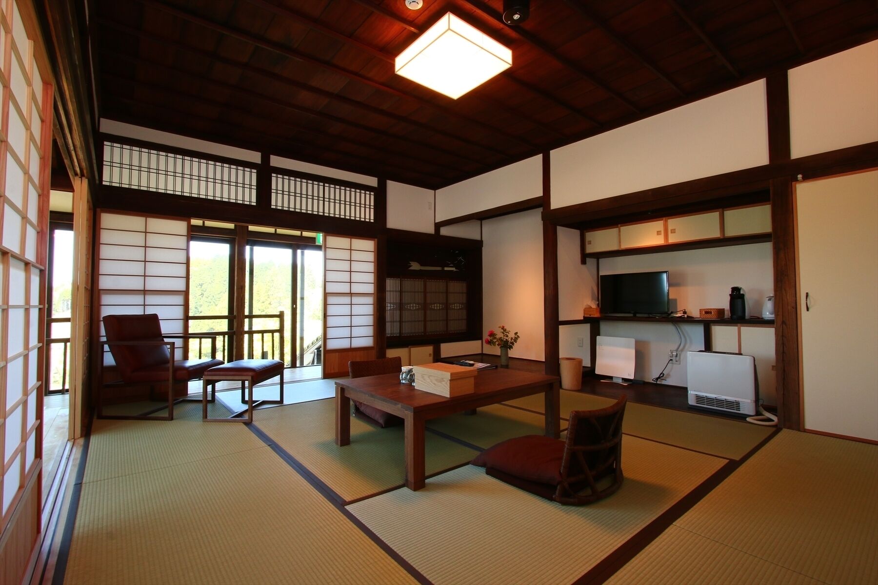 A traditional Japanese room with tatami flooring, a low table, a sofa, a television, and a heater.