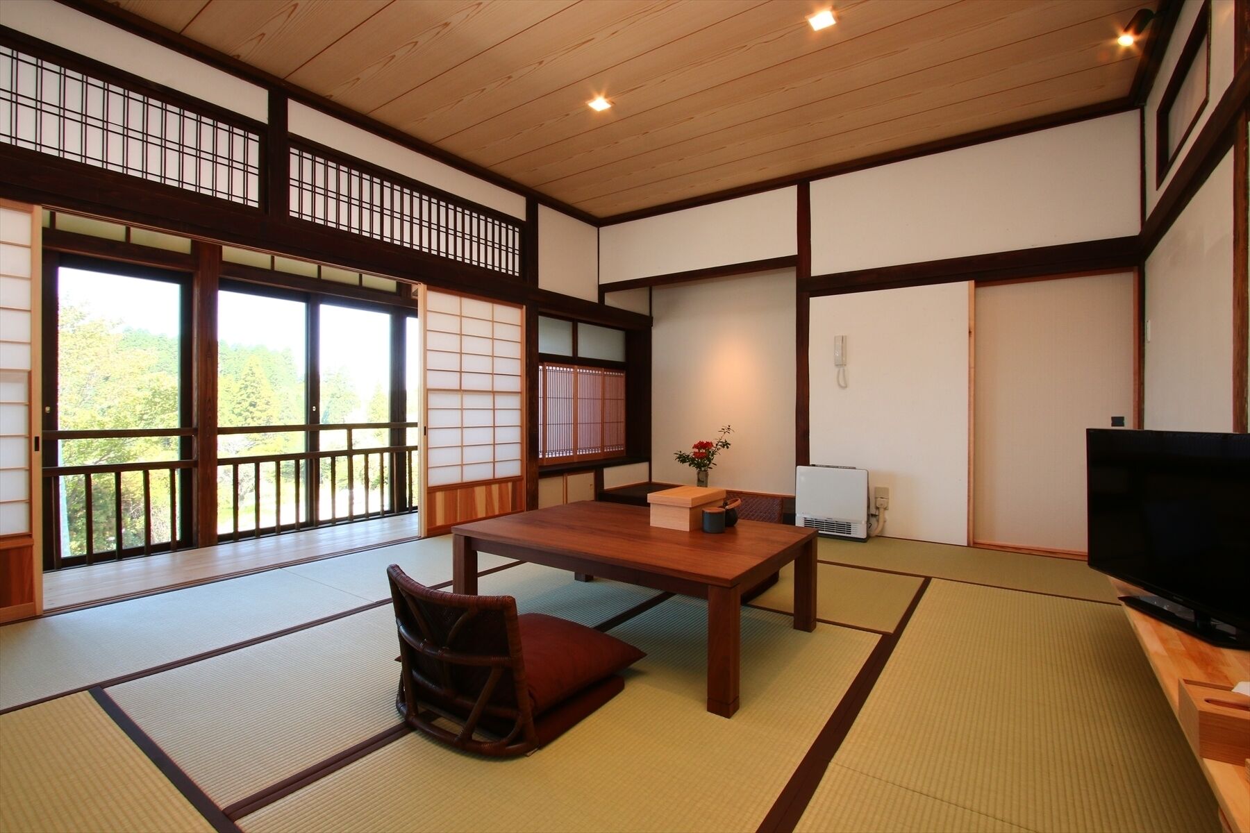 A traditional Japanese-style room with tatami flooring, a low wooden table, a television, and sliding doors.
