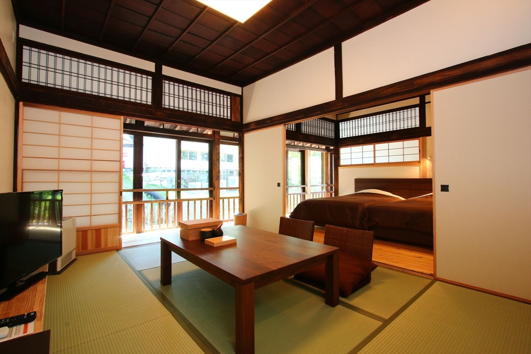 A traditional Japanese-style room with tatami flooring, a low wooden table, a bed with a wooden headboard, and sliding doors.