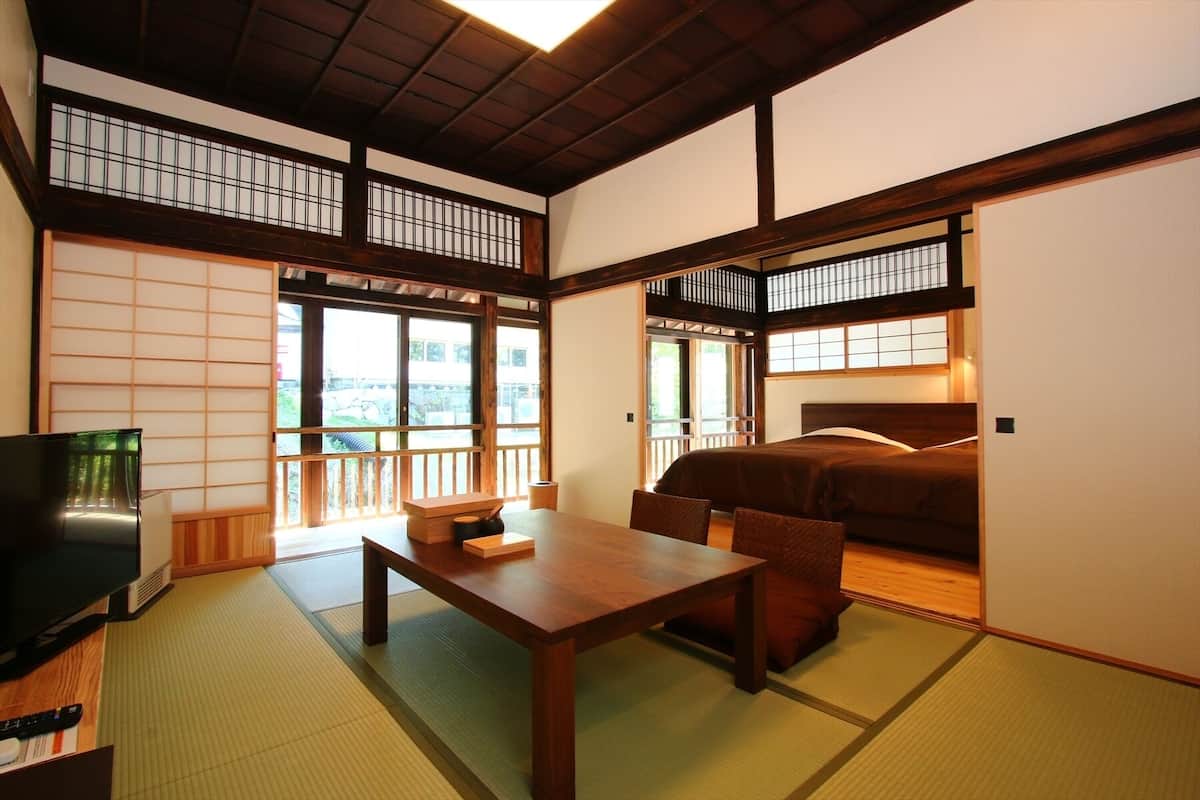 Una habitación tradicional japonesa con suelo de tatami, una mesa de madera baja, una cama con cabecero de madera y puertas correderas.