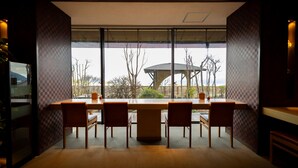 A dining area with a large table and chairs, large windows with blinds, and a view of trees and a gazebo outside. - Choubounoyado Shiori (Beppu)