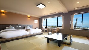 A hotel room with a large bed, a dining table, and a view of the city. - Choubounoyado Shiori (Beppu)
