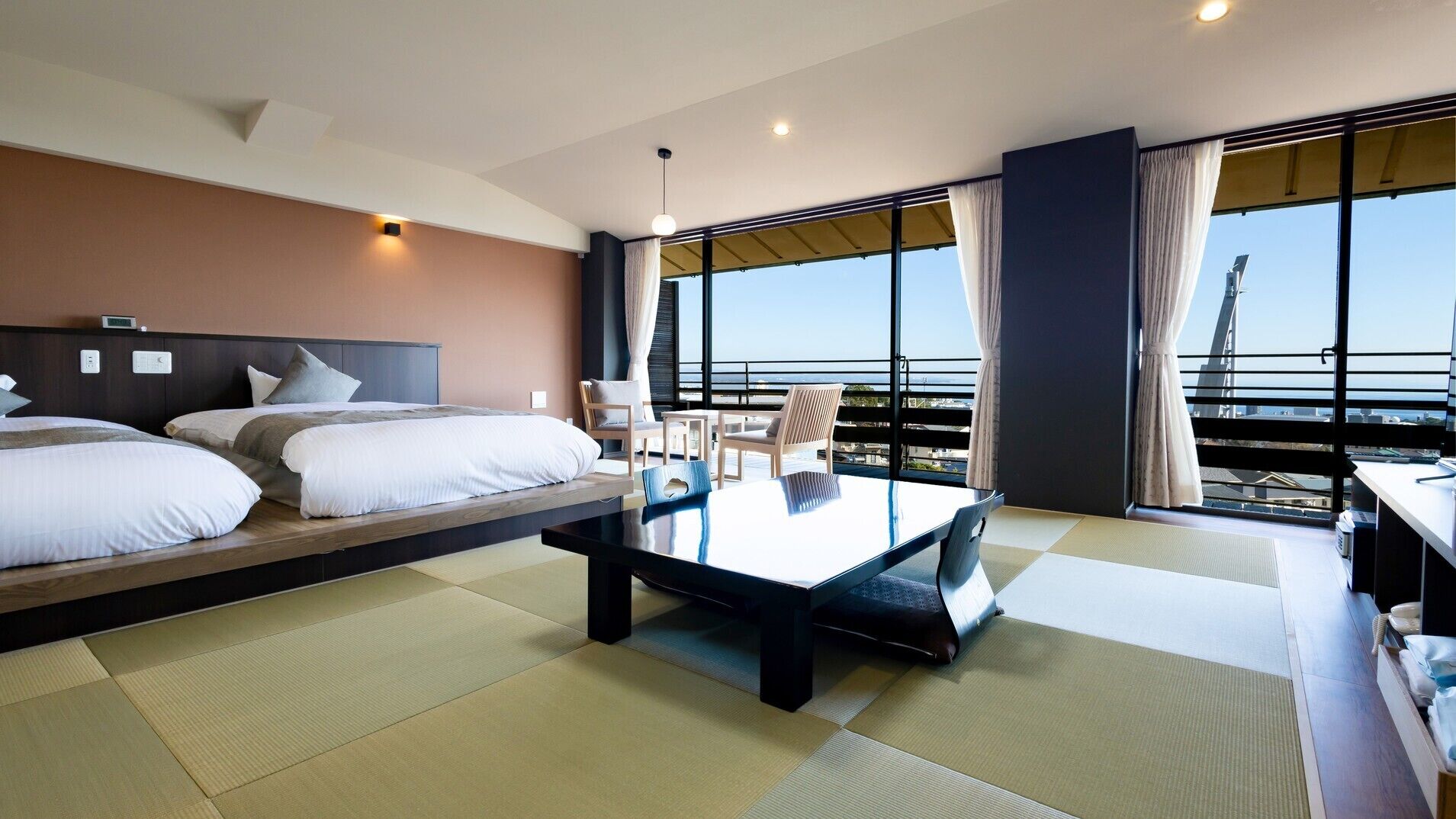 Habitación de hotel con dos camas, una mesa de comedor, sillas, vista a la ciudad y un balcón.