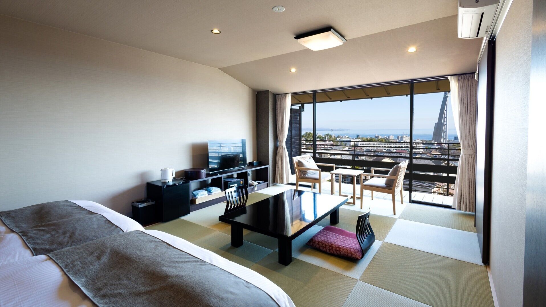 Habitación de hotel con cama, escritorio, televisor y balcón con vista a la ciudad.