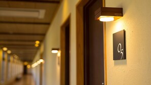 A hallway with illuminated wall sconces, a door with a number sign, and a ceiling with recessed lighting. - Fontana No Oka Kamo (Aira)