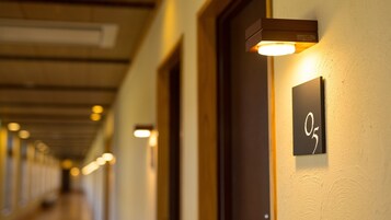 A hallway with illuminated wall sconces, a door with a number sign, and a ceiling with recessed lighting.