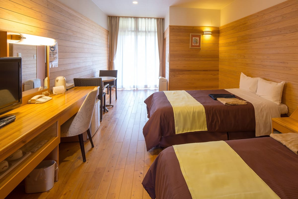 Una habitación de hotel con dos camas, un escritorio con teléfono, una silla y un televisor.