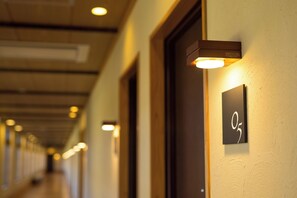 Un couloir d’hôtel avec des portes et des panneaux lumineux.