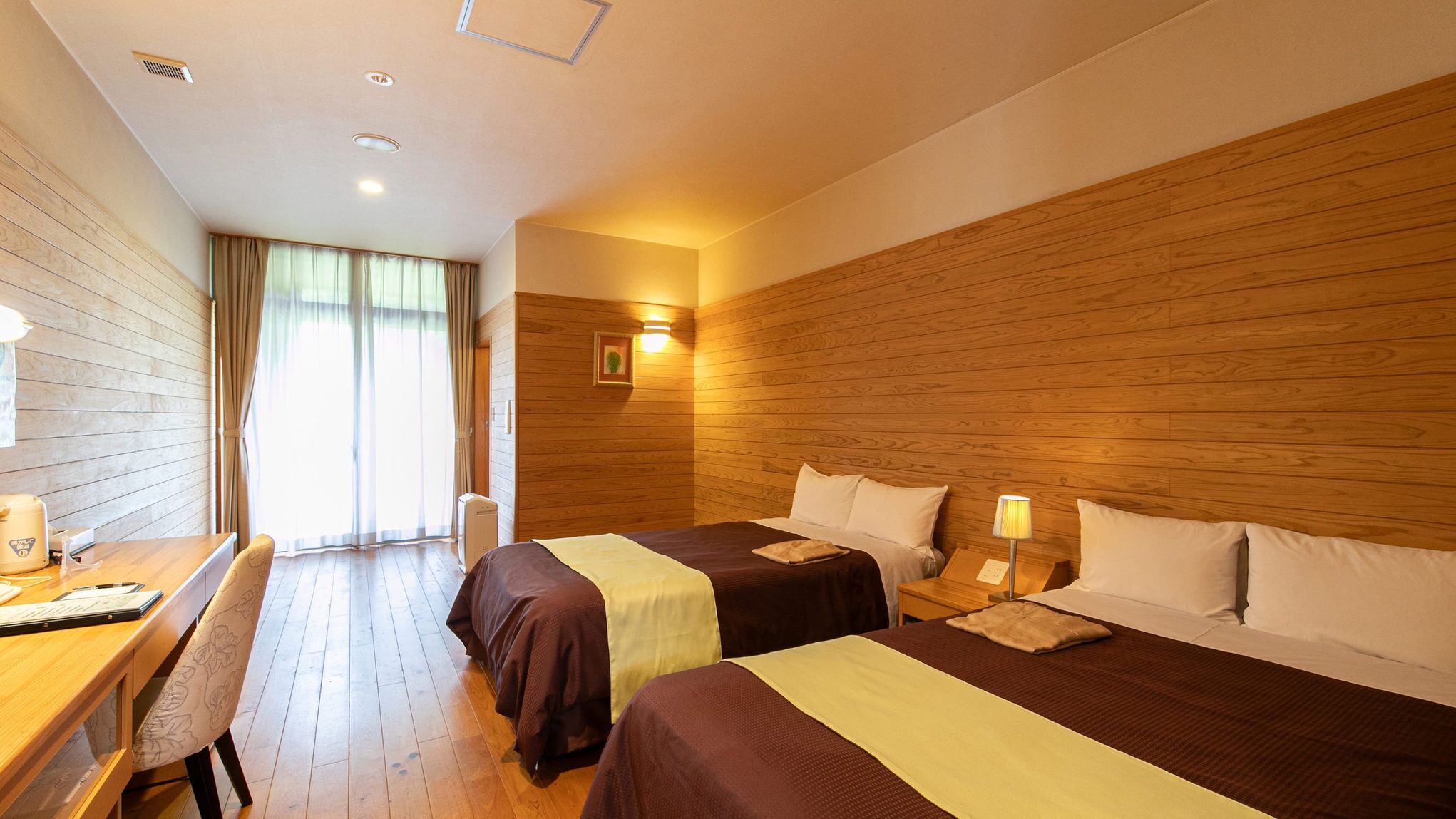 A hotel room with two beds, a desk, a chair, and a window with curtains.